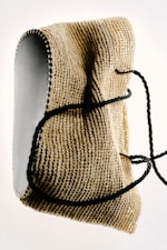 Placeholder for: Woven beige handbag with black string handles, featuring a textured surface and rounded white edges, against a light background.