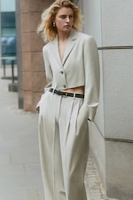Placeholder for: Person standing wearing beige crop suit jacket and suit trousers