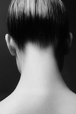 Placeholder for: Black and white close-up of the back of a person's head and neck with neatly slicked-back hair.