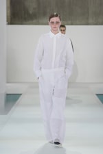 Placeholder for: Model in white, oversized shirt and pants walking on a runway with a minimalist background.