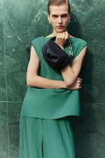 Placeholder for: Person wearing orange sunglasses, green pleated top holding black leather bag