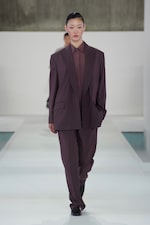 Placeholder for: Person walking on a runway wearing an oversized brown suit with a matching shirt, against a minimalist background.
