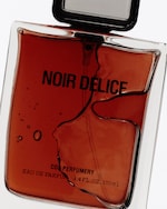 Placeholder for: A rectangular glass bottle of Noir Délice Eau de Parfum, filled with amber liquid, featuring a bold black cap and minimalist design.