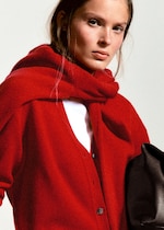 Placeholder for: A person wearing a red cardigan with a white top underneath, a red scarf draped over their shoulders, and holding a black bag.