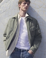 Placeholder for: Man in a white vest over a green shirt resting on a wall