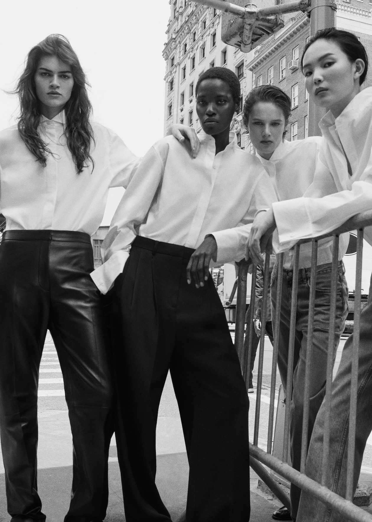Four models wearing white shirts and wide-leg pants pose confidently in an urban setting with a historic building in the background.