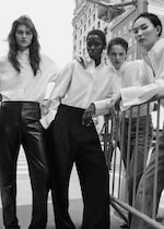 Placeholder for: Four models wearing white shirts and wide-leg pants pose confidently in an urban setting with a historic building in the background.
