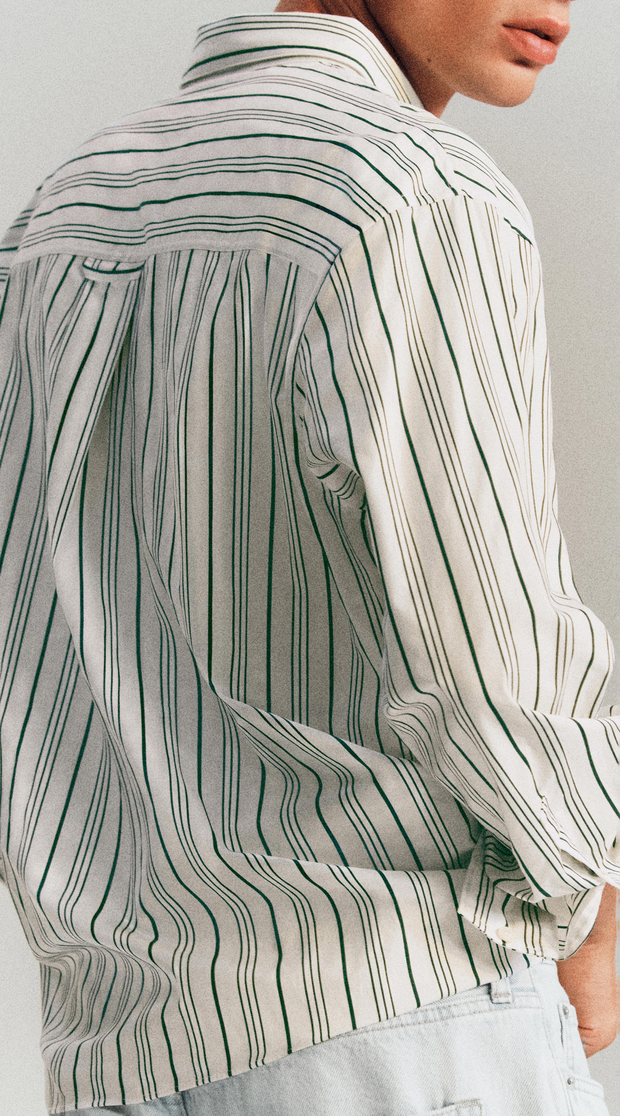 A person wearing a loose-fitted, long-sleeve, striped shirt in white and black. The shirt has a casual and comfortable style.