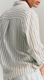 Placeholder for: A person wearing a loose-fitted, long-sleeve, striped shirt in white and black. The shirt has a casual and comfortable style.