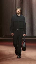 Placeholder for: Man wears black shirt, black pants and holds black bag