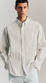 Placeholder for: Man wearing a white shirt with green stripes, standing with hands in light pants pockets.