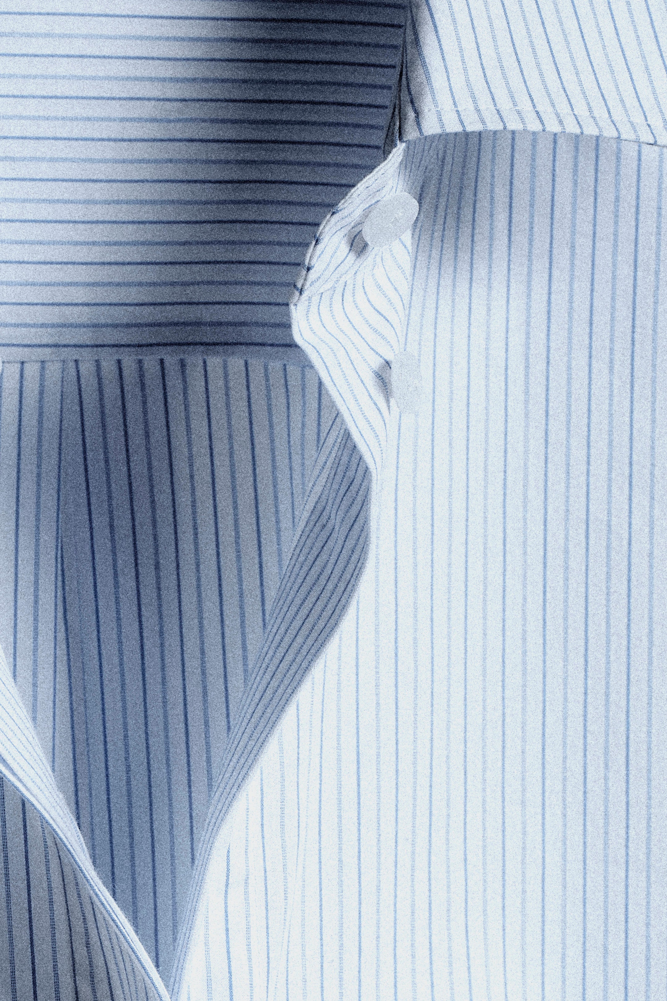 Close-up of a blue and white striped shirt with visible buttons and overlapping fabric, showing sharp texture and crisp lines.