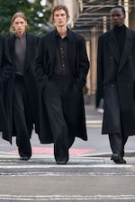 Placeholder for: Three individuals in long black coats and dark clothing walking confidently on a city street.