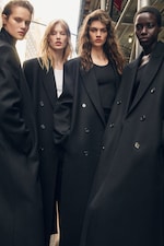 Placeholder for: Four models in black long coats pose confidently in an urban setting.