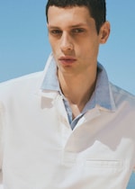 Placeholder for: Man in a white shirt with a blue collar stands against a clear blue sky, exuding a calm and thoughtful demeanor.