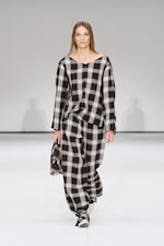 Placeholder for: A model walks the runway wearing a loose-fitting black and white plaid outfit, holding a small bag, against a plain background.