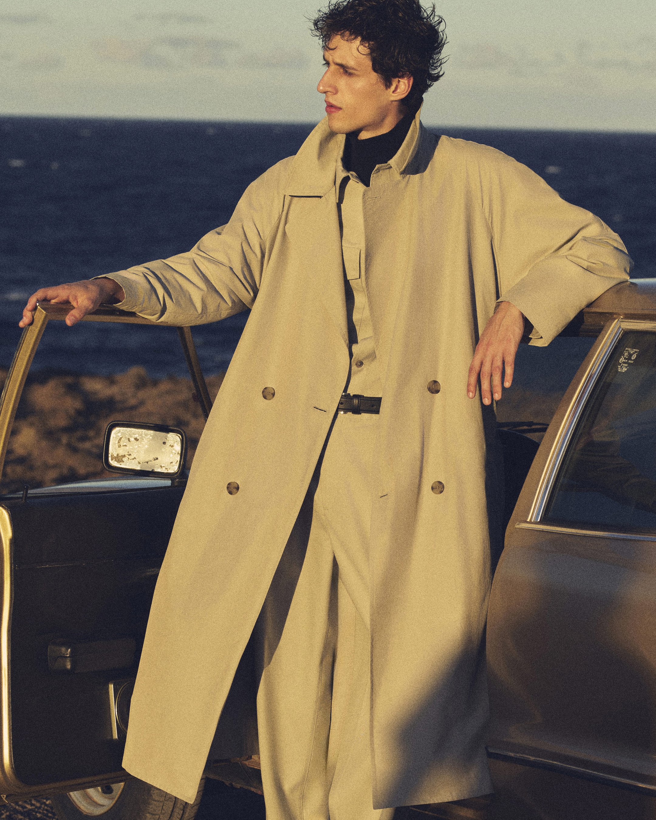 Man in a mac jacket hanging above a car door