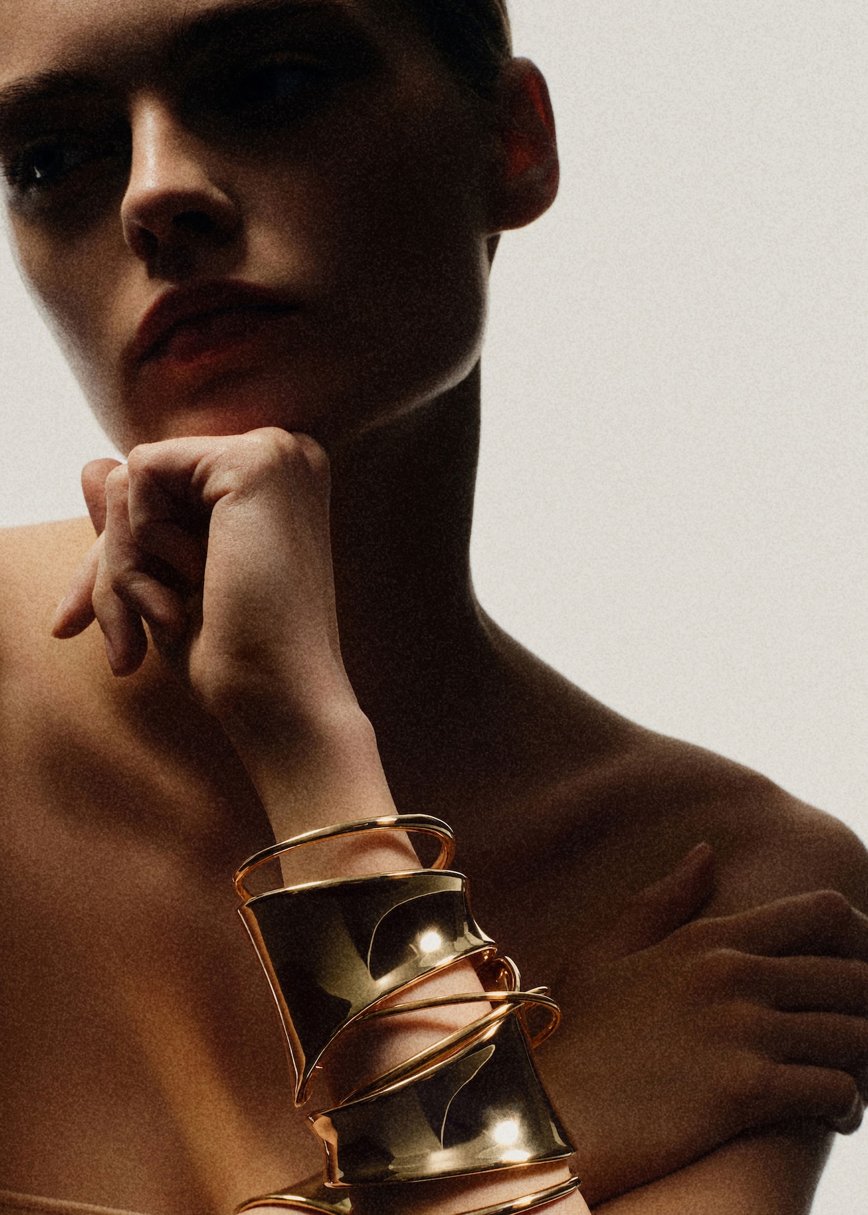 Silhouetted person with hand on chin, wearing multiple gold bangles on forearm, against a light background.