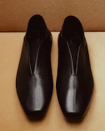 Placeholder for: A pair of sleek black leather loafers with square toes and visible stitching, placed side by side on a light brown surface.