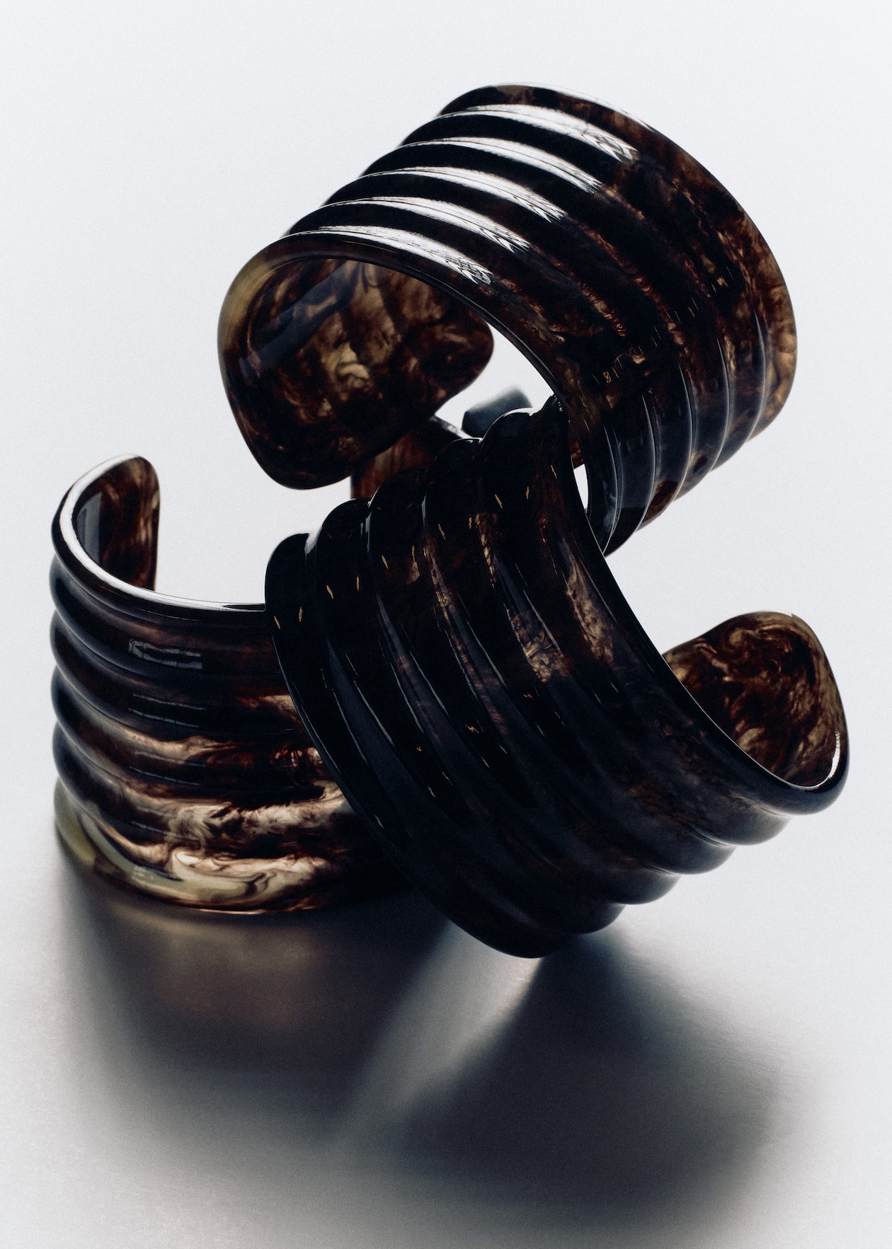 Two dark, intricately carved resin bangles with a swirling pattern, stacked on a reflective surface.