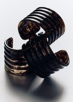 Placeholder for: Two dark, intricately carved resin bangles with a swirling pattern, stacked on a reflective surface.