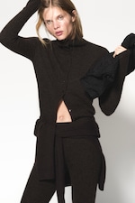 Placeholder for: Person wearing a dark brown cardigan and pants, holding a black fabric piece. The cardigan is partly open, revealing a glimpse of their midriff.