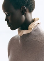 Placeholder for: Profile of a person wearing a gray turtleneck sweater and a light-colored scarf, looking down against a soft, blurred background.