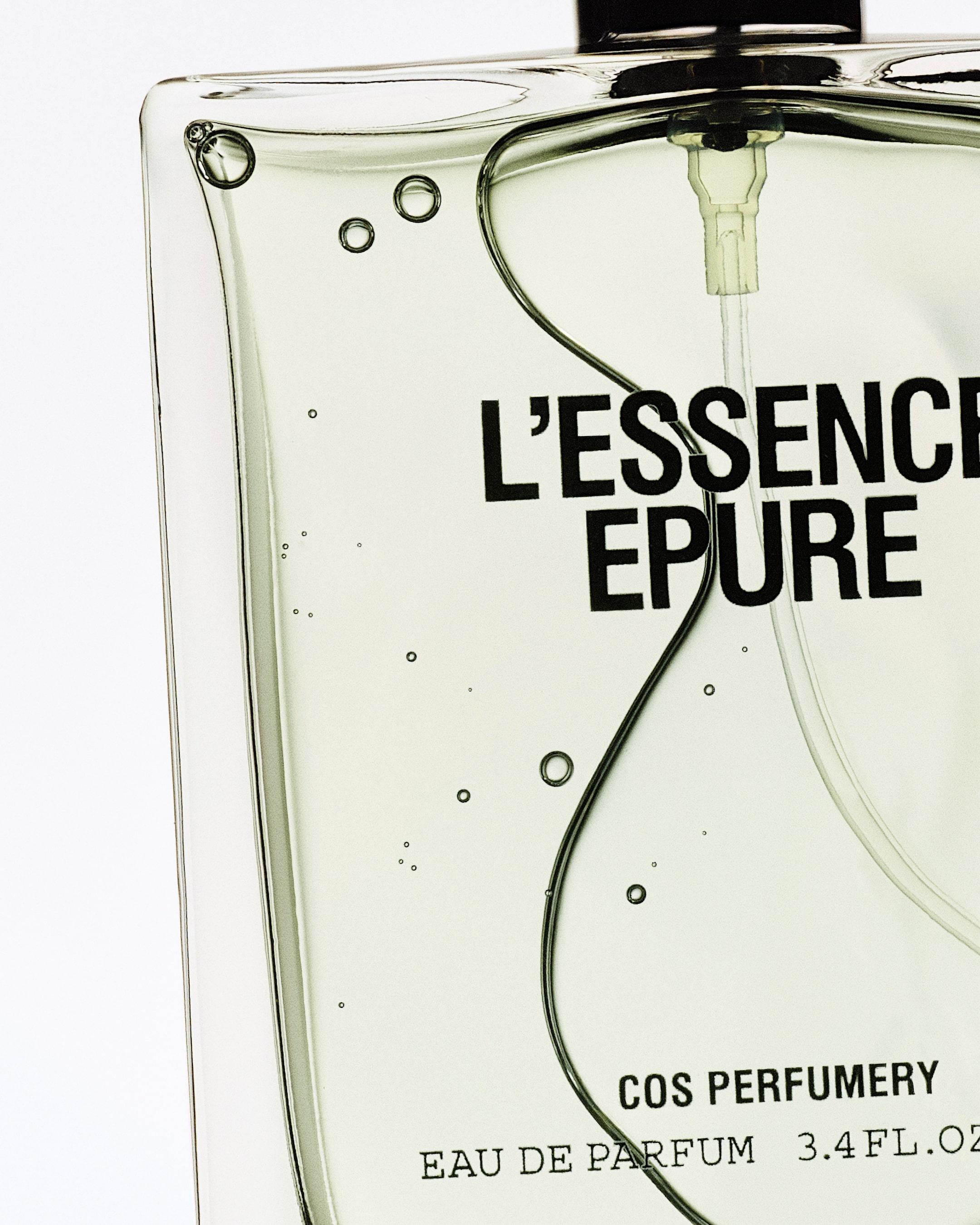 Close-up of a perfume bottle labeled "L'Essence Epure" by COS Perfumery, showing clear liquid with air bubbles inside.