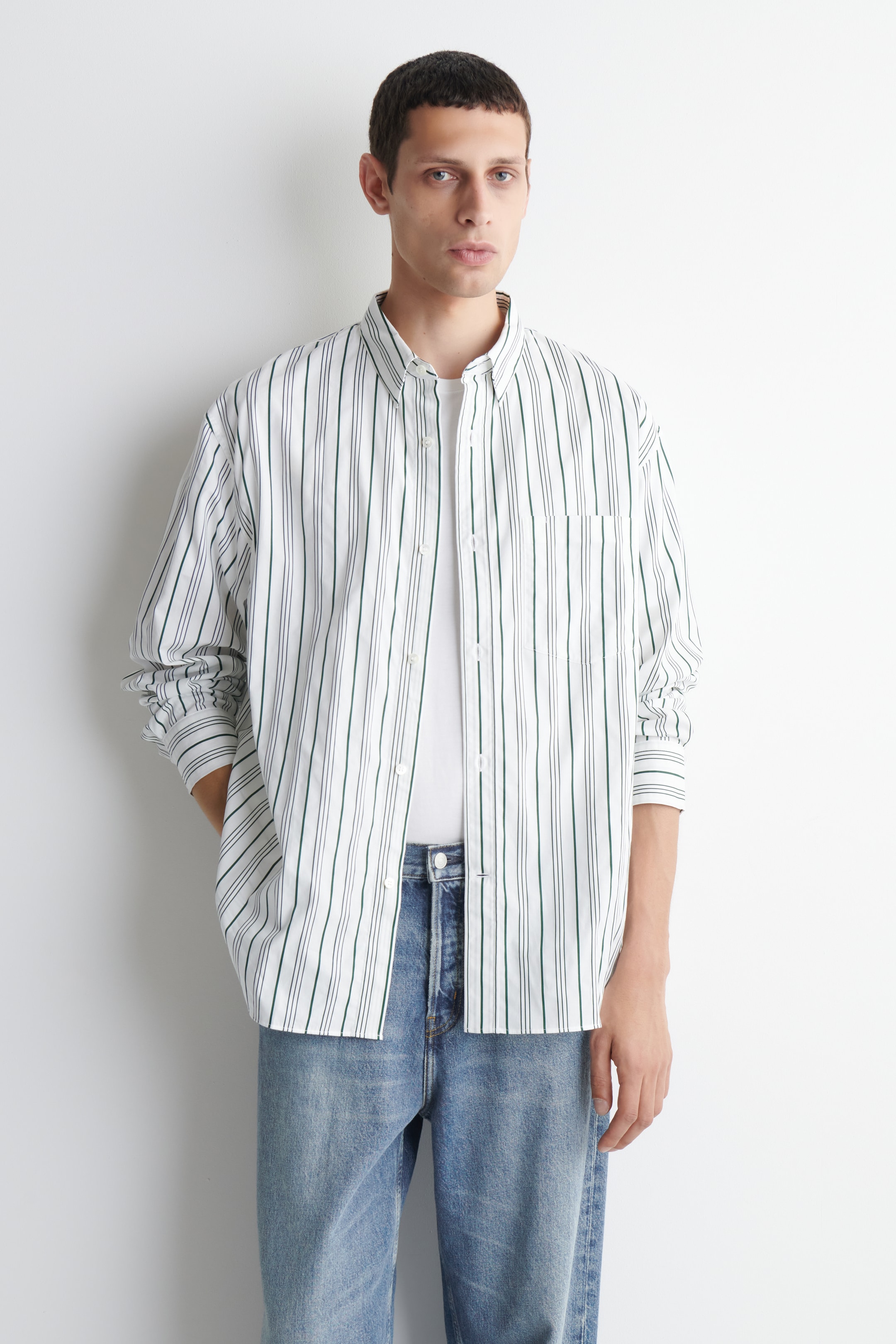 Person wearing a white shirt with black stripes, white undershirt, and blue jeans, standing against a plain white background.