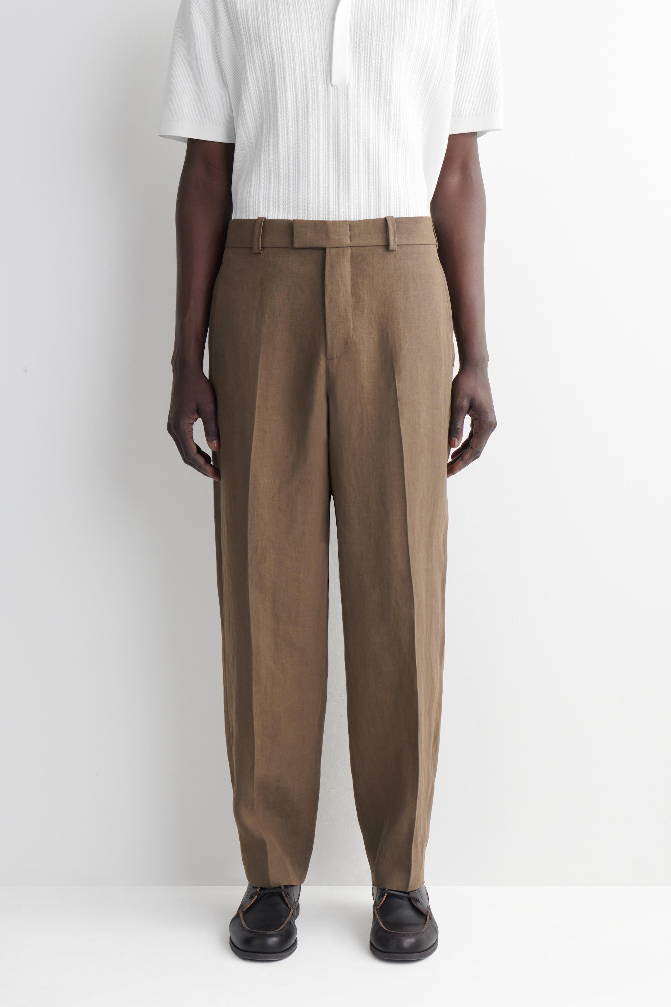 Person wearing a white short-sleeve shirt, brown pants, and black shoes, standing against a plain white background.