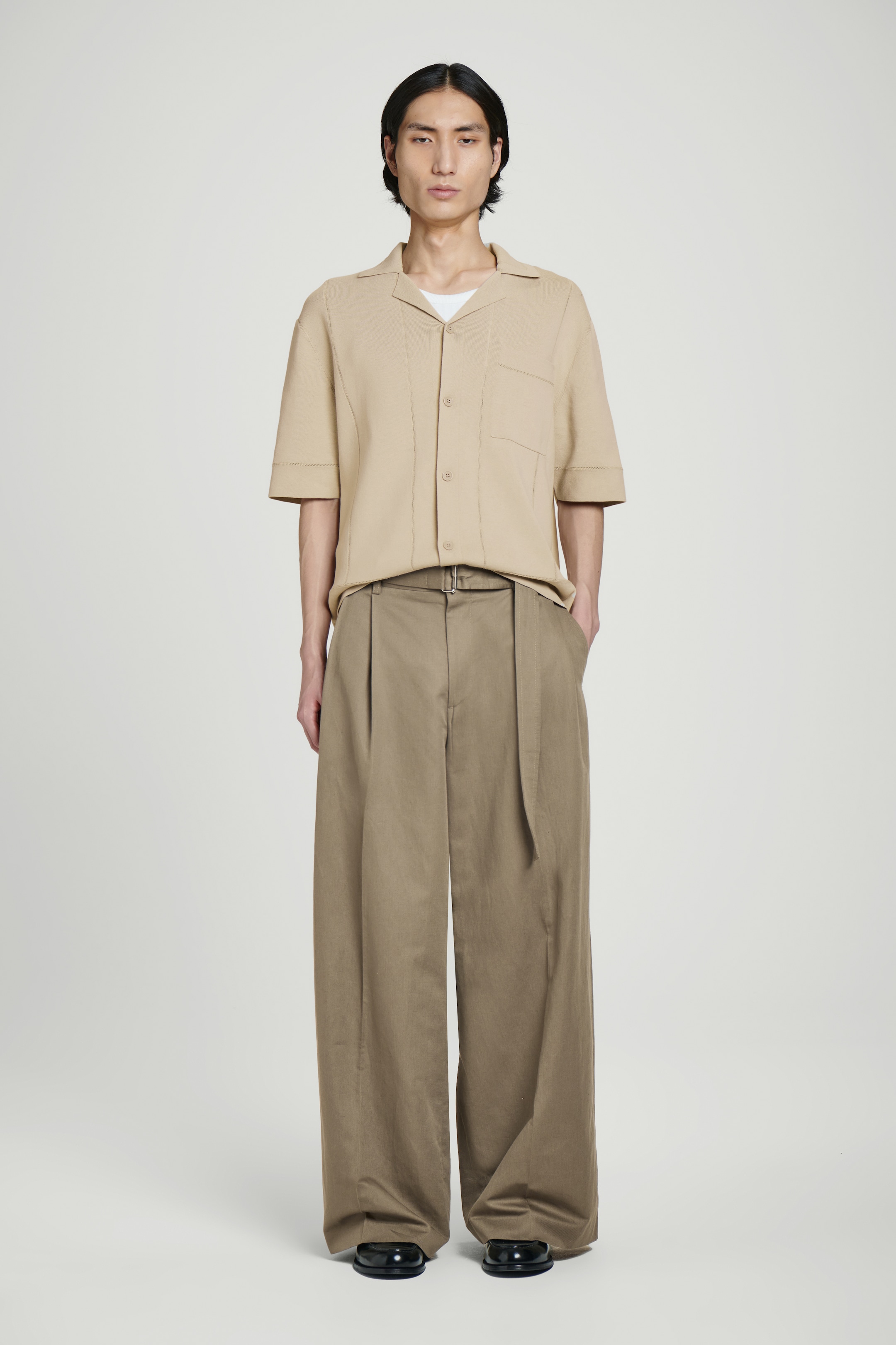 Person wearing a beige short-sleeve shirt with a pocket and wide-leg khaki pants, standing against a plain white background.