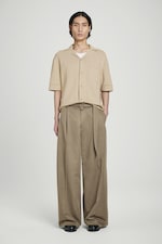 Placeholder for: Person wearing a beige short-sleeve shirt with a pocket and wide-leg khaki pants, standing against a plain white background.