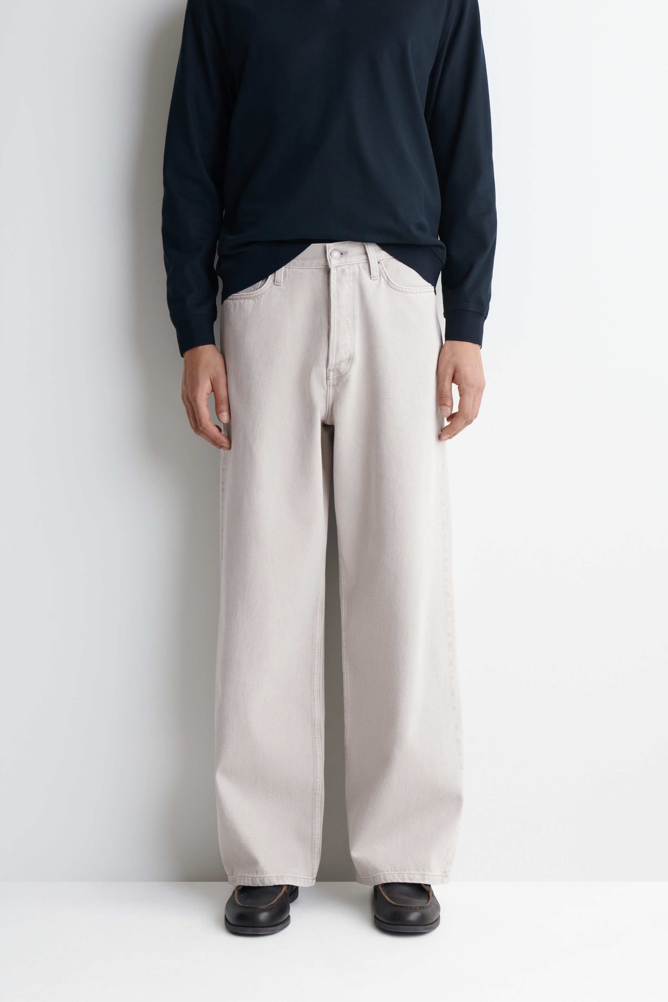 Person wearing a black long-sleeve shirt, light gray wide-leg pants, and black shoes, standing against a white background.