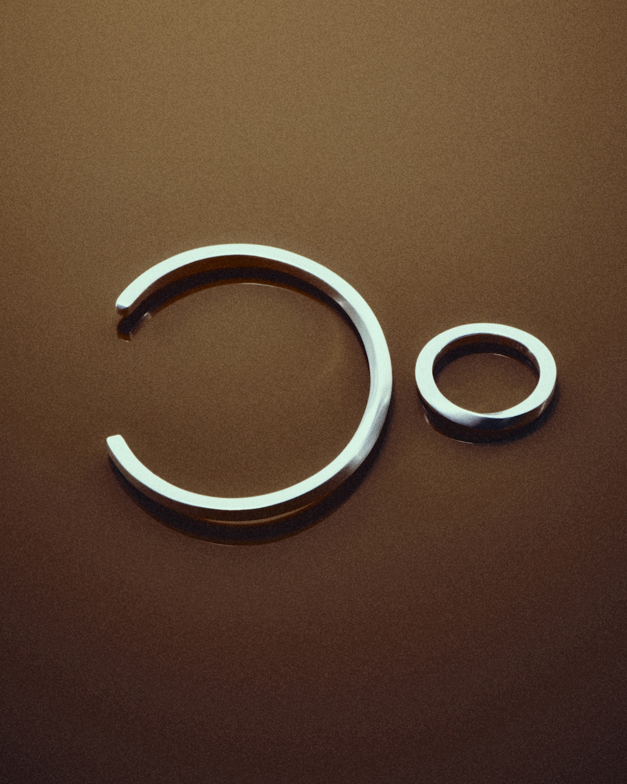Two silver rings on a brown surface, one larger and open, the other smaller and closed, arranged to resemble a minimalist face.