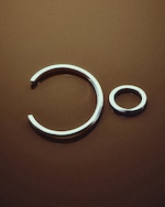 Placeholder for: Two silver rings on a brown surface, one larger and open, the other smaller and closed, arranged to resemble a minimalist face.