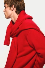 Placeholder for: Person in profile wearing a bright red sweater with a matching scarf draped over their shoulders against a plain background.