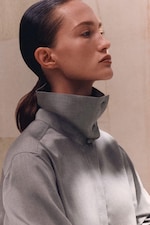 Placeholder for: Profile of a person with sleek hair tied back, wearing a high-collared gray shirt against a neutral background.