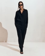 Placeholder for: A person in a black outfit and sunglasses walks confidently against a plain background.