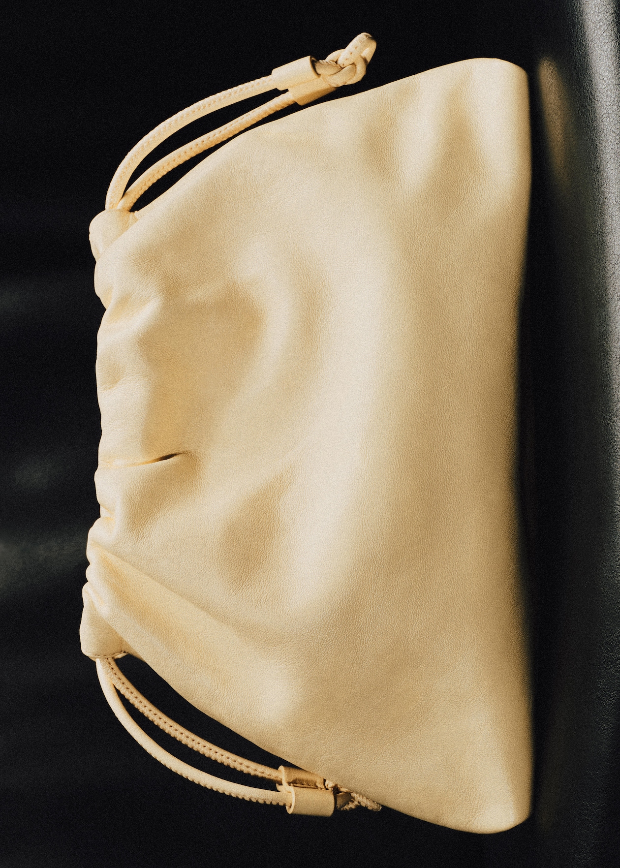 A beige drawstring pouch lying on a dark surface, showcasing its soft leather texture and simple design.