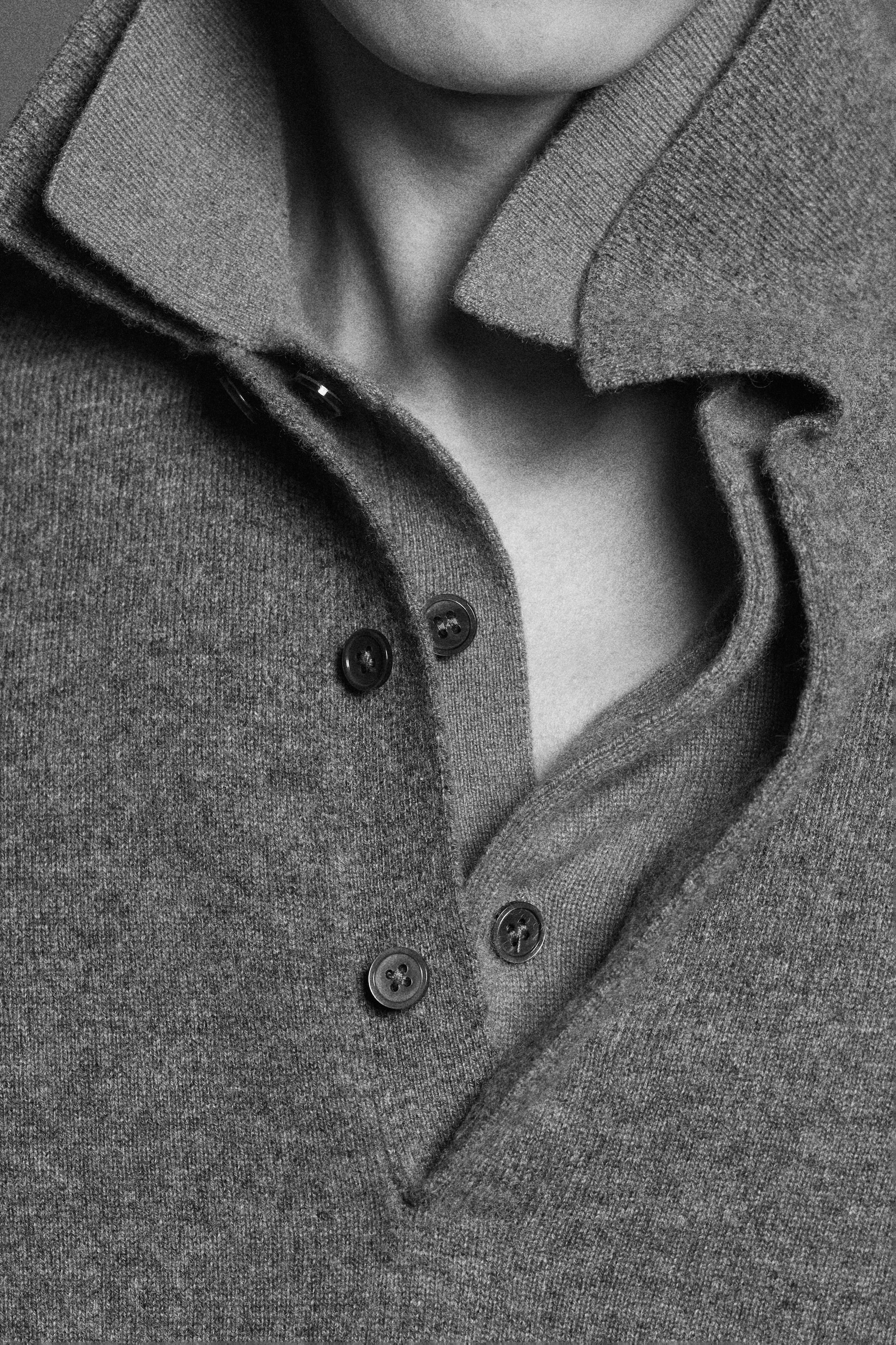 Close-up of a person's neck and shoulders wearing a textured, buttoned gray sweater with a folded collar, in black and white.