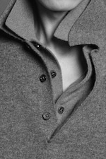 Placeholder for: Close-up of a person's neck and shoulders wearing a textured, buttoned gray sweater with a folded collar, in black and white.