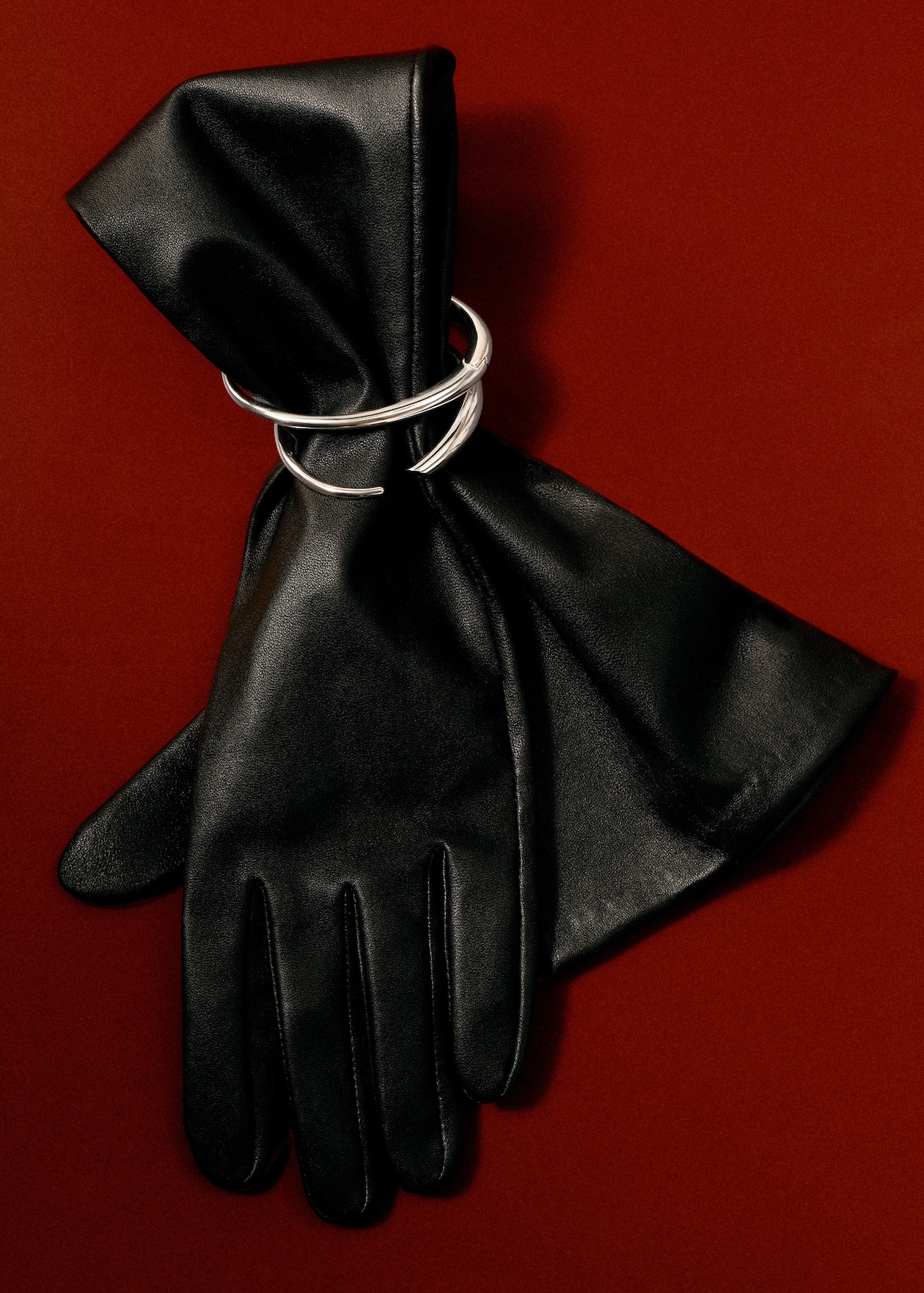 Black leather gloves adorned with a silver cuff bracelet against a rich red background.