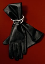 Placeholder for: Black leather gloves adorned with a silver cuff bracelet against a rich red background.