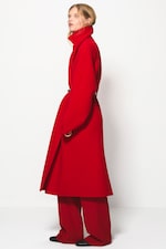 Placeholder for: Person wearing a long red coat with matching wide-leg pants, standing against a plain white background.