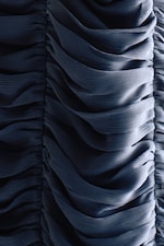 Placeholder for: Close-up of dark blue, pleated fabric showcasing intricate textures and folds, with light creating subtle highlights.