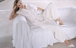 Placeholder for: Woman in a stylish, all-white outfit reclines on a white sofa, exuding elegance and sophistication in a minimalist setting.