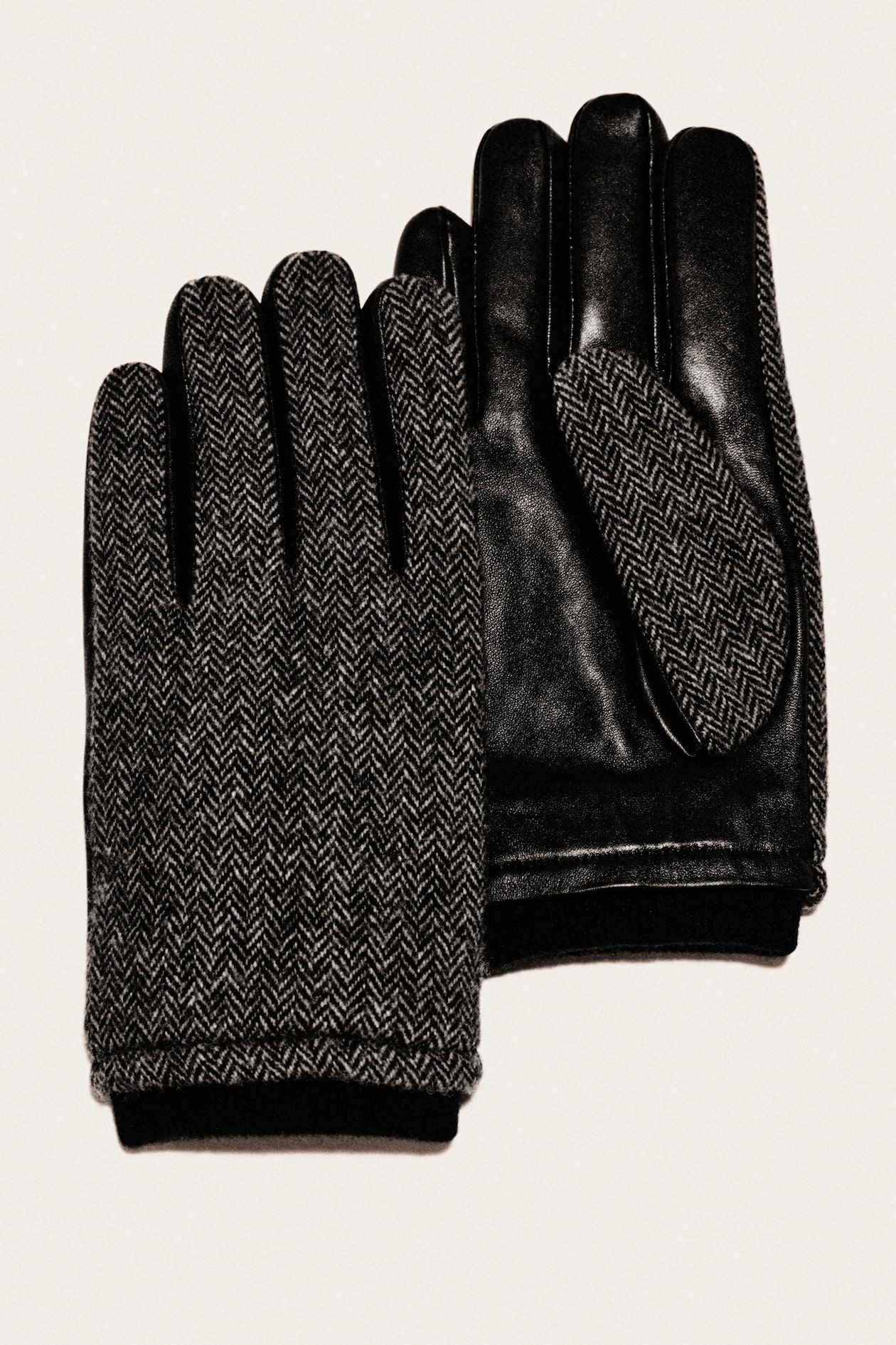 Pair of black gloves: one herringbone wool top, one smooth leather palm with matching herringbone thumb patch, on a light background.