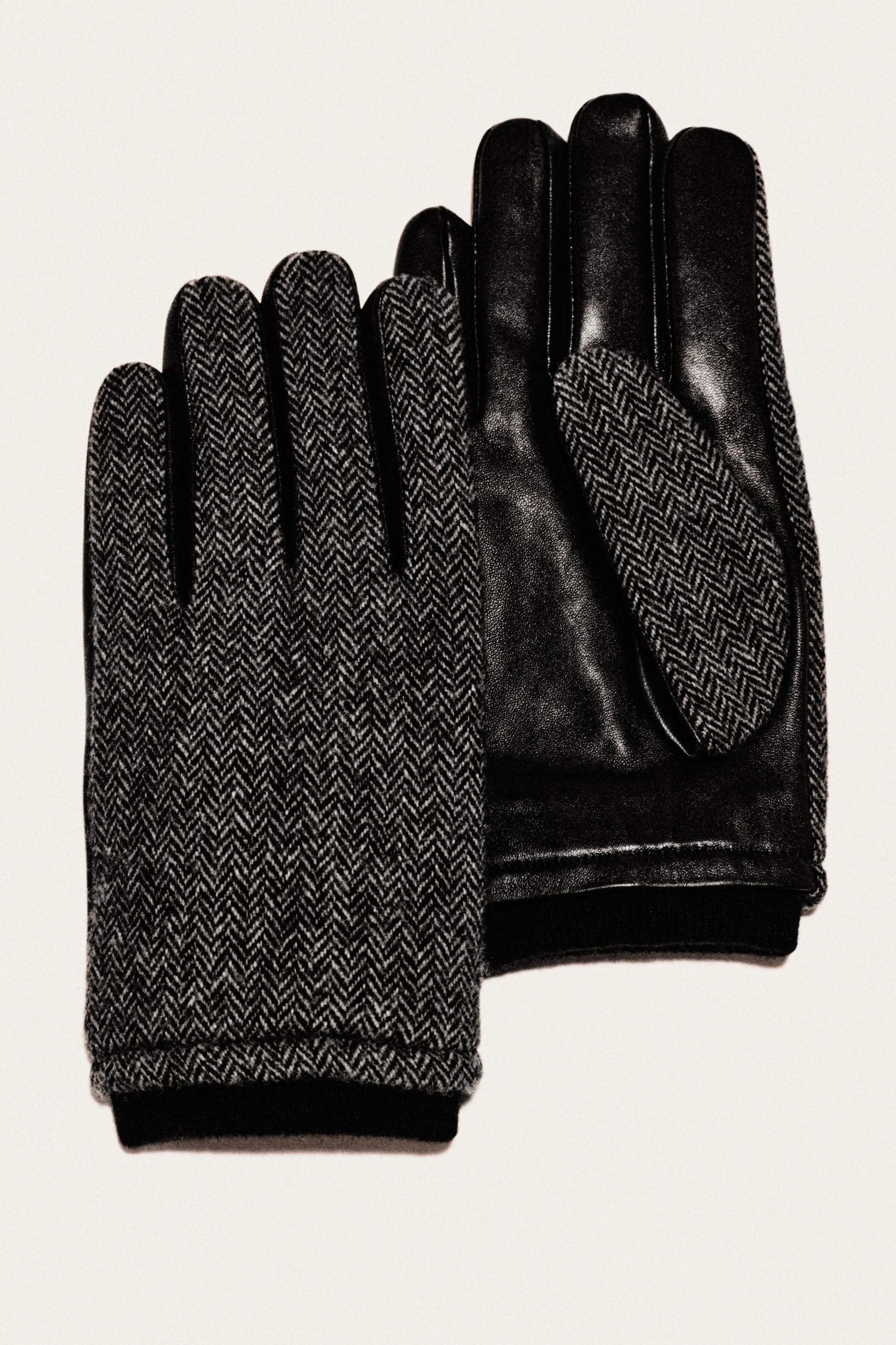 Pair of black gloves: one herringbone wool top, one smooth leather palm with matching herringbone thumb patch, on a light background.