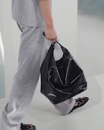 Placeholder for: Person in light gray outfit walking, holding a large black leather bag.