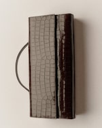 Placeholder for: A rectangular, brown crocodile-patterned leather clutch with a handle, placed on a light surface.